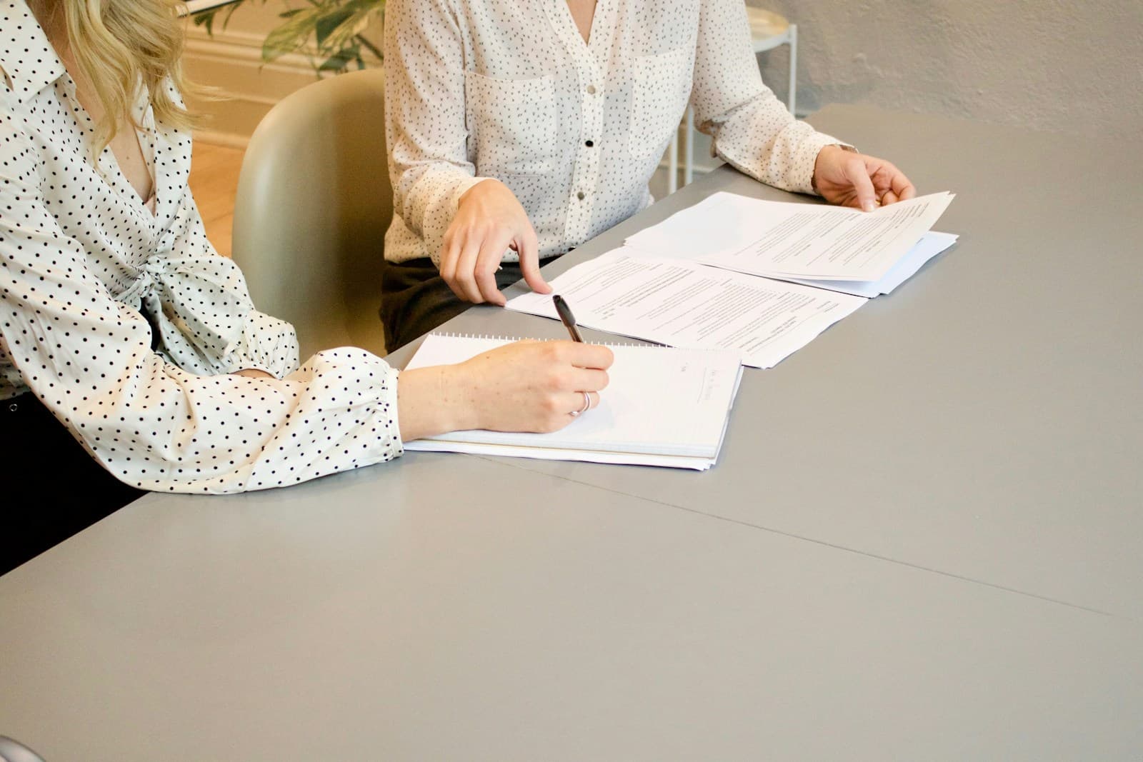 Two women at a light table, one writing on documents while the other reviews them