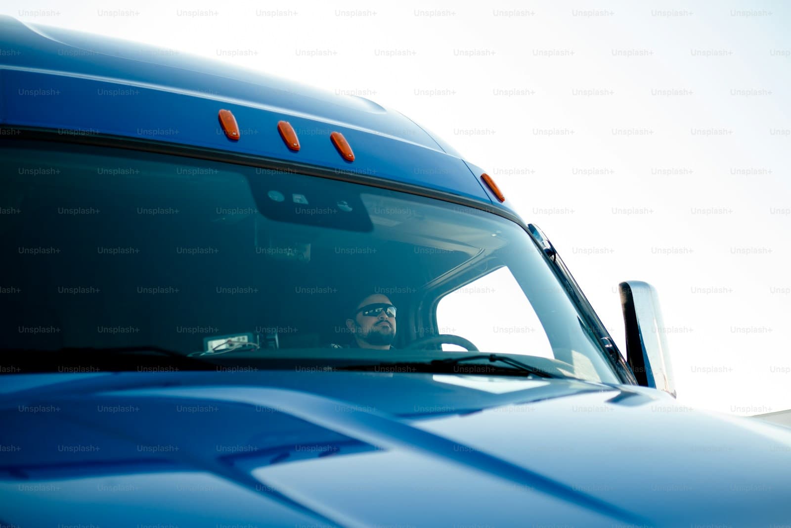 Truck driver in glasses behind the windshield of a blue semi cab