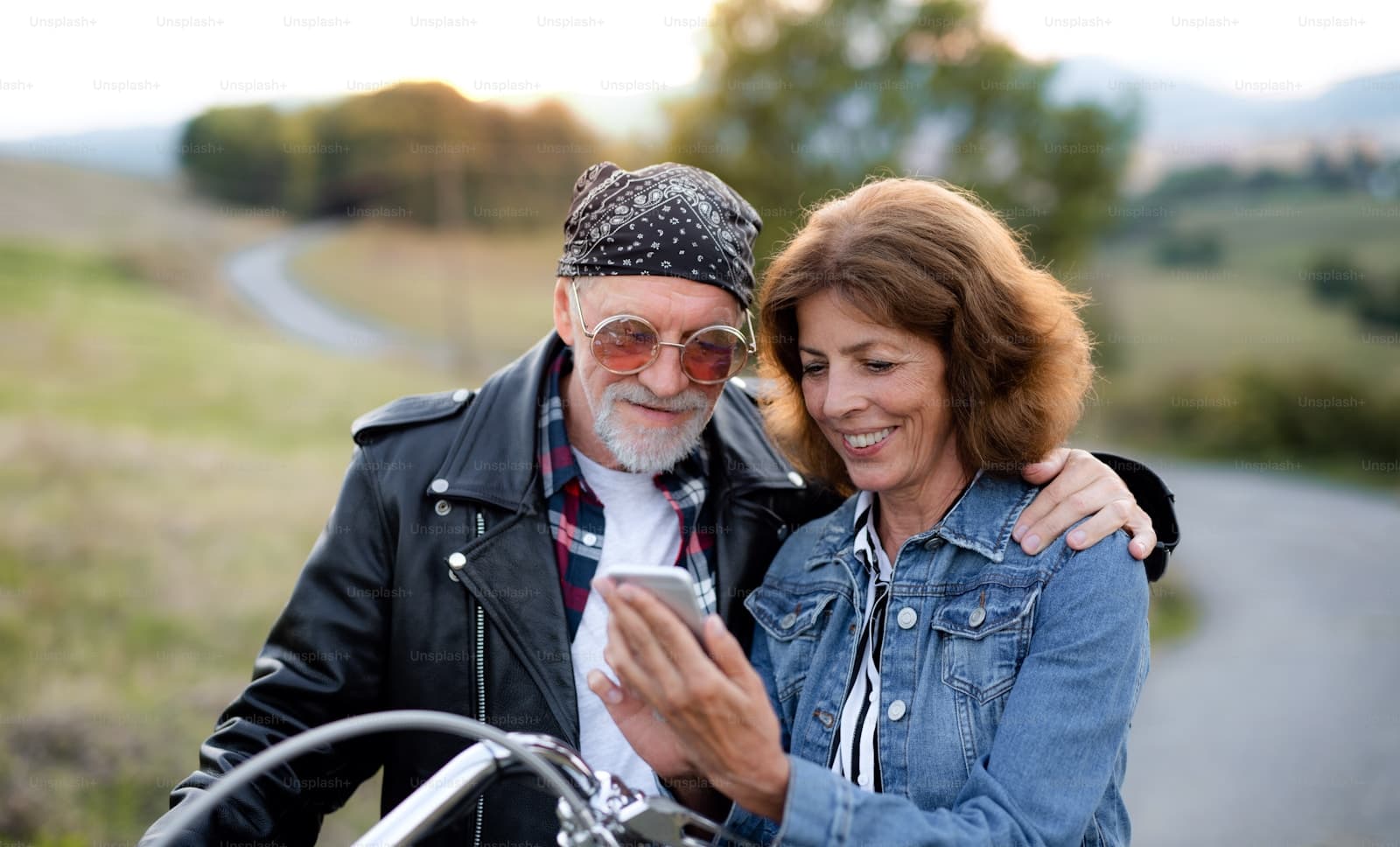 Middle-aged couple outdoors sharing a smartphone screen, the man in sunglasses and a bandana