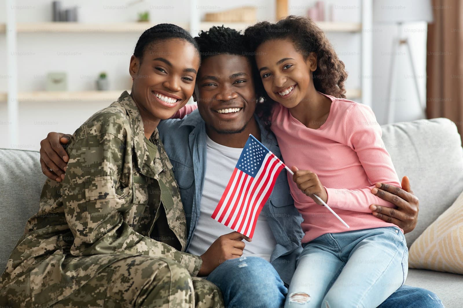 Three people on a living-room couch, one in military uniform, smiling together