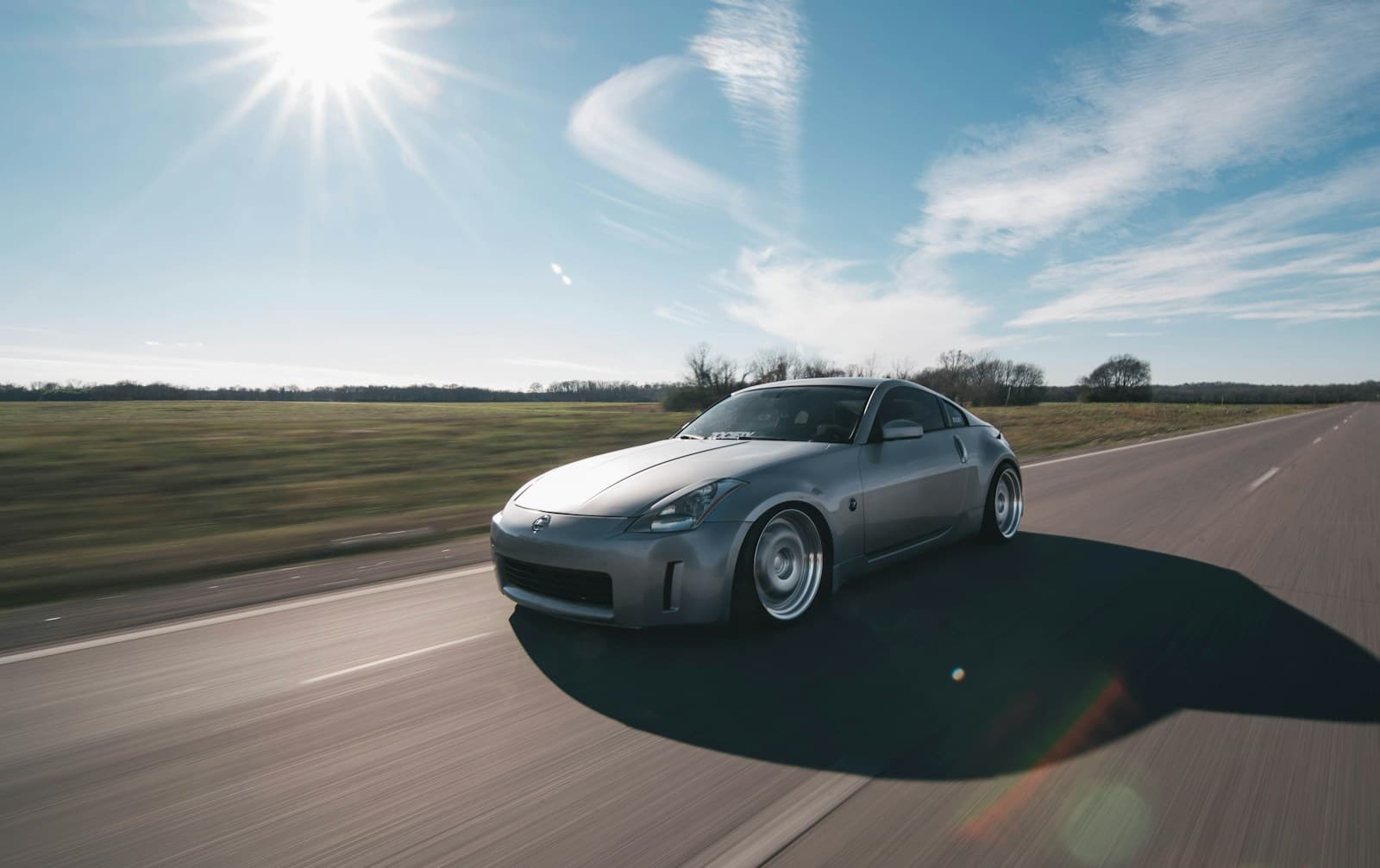 Silver sports car on an empty countryside road under a bright sunny sky